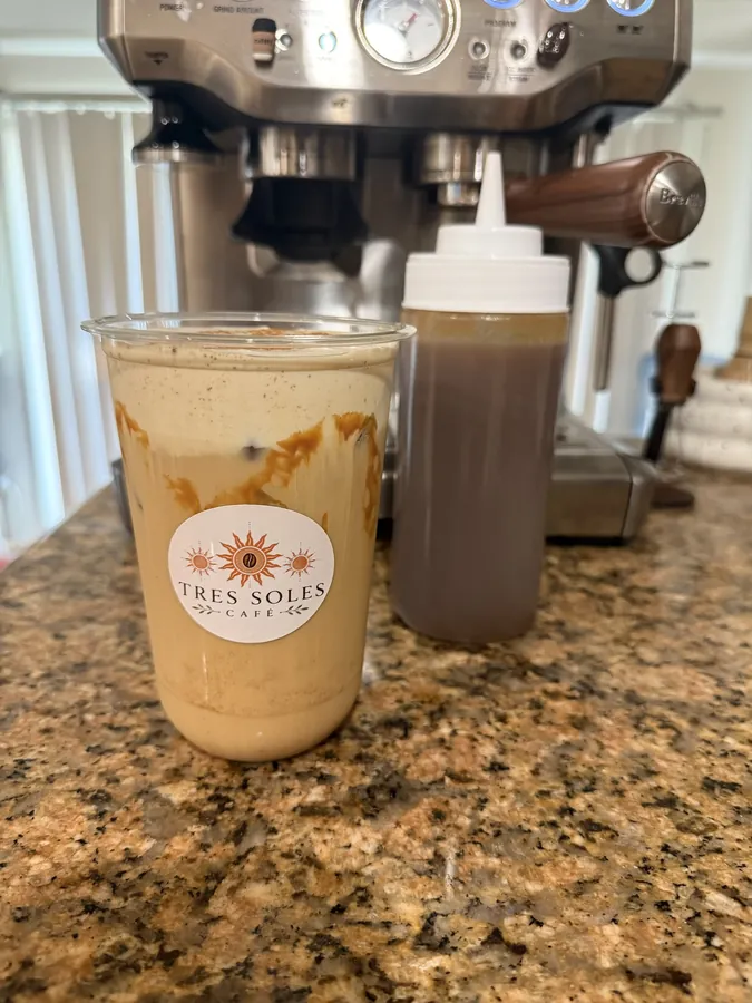 An iced latte with a Tres Soles sticker in front of the espresso machine